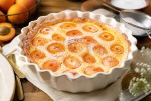 Aprikosen-Clafoutis frisch aus dem Ofen, goldbraun gebacken in einer runden Auflaufform, mit Puderzucker bestäubt