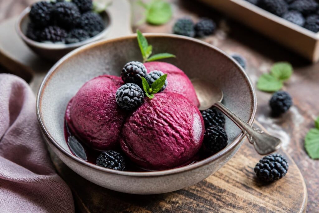 Brombeer-Sorbet ohne Eismaschine in einer weißen Schale, cremig und tiefviolett, garniert mit frischen Brombeeren und Minzblättern