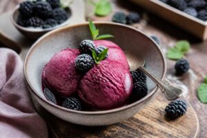 Brombeer-Sorbet ohne Eismaschine in einer weißen Schale, cremig und tiefviolett, garniert mit frischen Brombeeren und Minzblättern