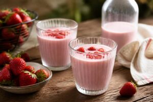 Erdbeermilch nach Omas Rezept im hohen Glas mit frischen Erdbeeren und Minze, von oben fotografiert auf hellem Holztisch