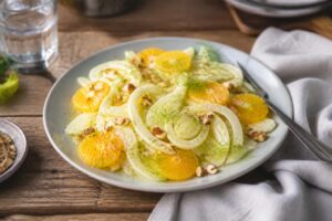Kalter Fenchel-Orangen-Salat auf einem hellen Teller, dünn gehobelt, mit Orangenfilets und roten Zwiebeln, beträufelt mit einer Honig-Senf-Marinade