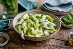 Kalter Zucchini-Salat mit Joghurt in einer weißen Schüssel, garniert mit frischer Minze und einem Spritzer Zitrone, von oben fotografiert
