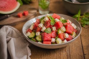 Wassermelonen-Gurken-Salat mit Feta, Minze und Limettendressing in einer weißen Schüssel auf hellem Holzuntergrund