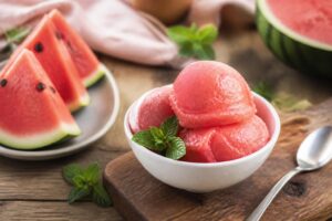 Cremiges Wassermelonen-Sorbet ohne Eismaschine in einer Schale, garniert mit frischer Minze und Limettenscheibe, fotografiert von oben