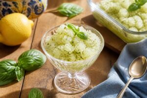 Zitronen-Basilikum-Granita in einer ausgehöhlten Zitronenschale serviert, mit frischen Basilikumblättern garniert, auf einem hellen Holztisch