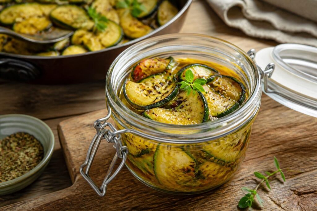 Zucchini-Antipasti aus der Pfanne mit Knoblauch, Olivenöl und Weißweinessig, angerichtet in einem Einmachglas auf einem Holzbrett